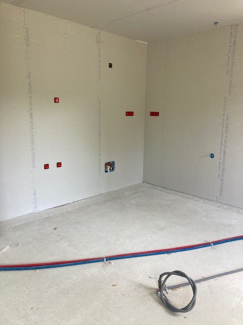 Préparation de l'installation électrique en rénovation Gaines électriques rouges et bleues posées au sol dans une pièce en rénovation.