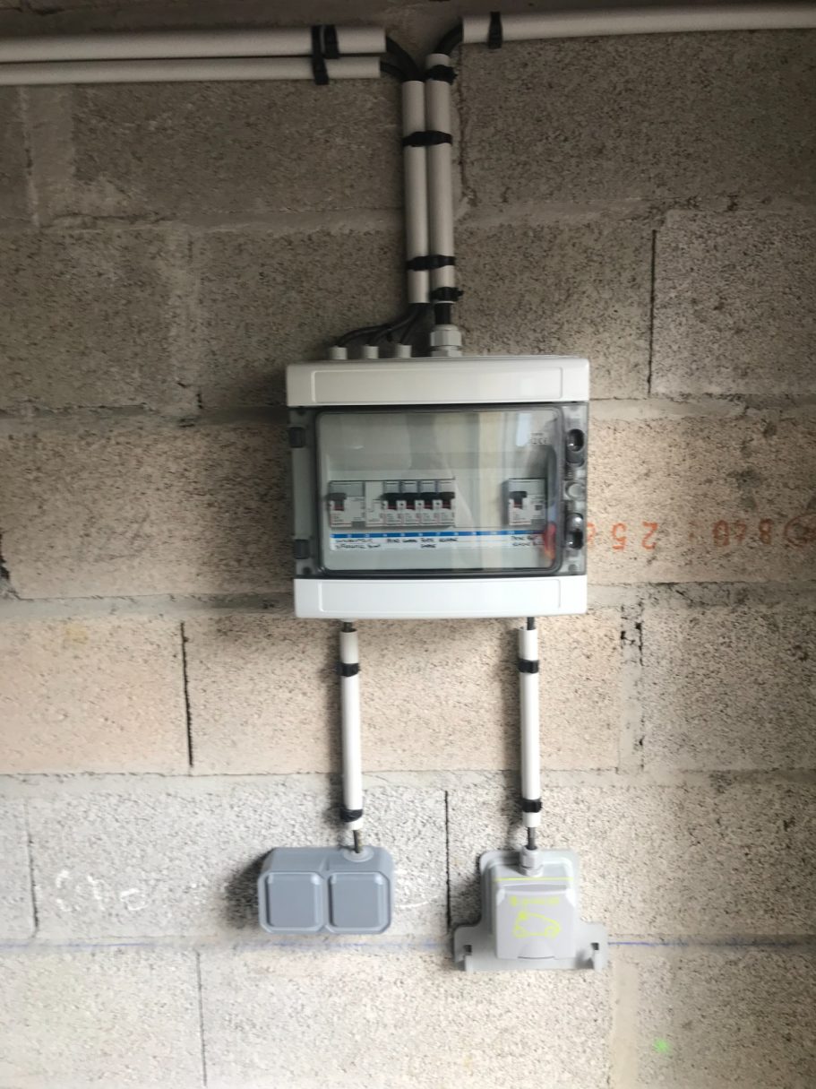 Pose d'un coffret électrique apparent Coffret électrique apparent fixé sur un mur en parpaings avec des conduits de protection.